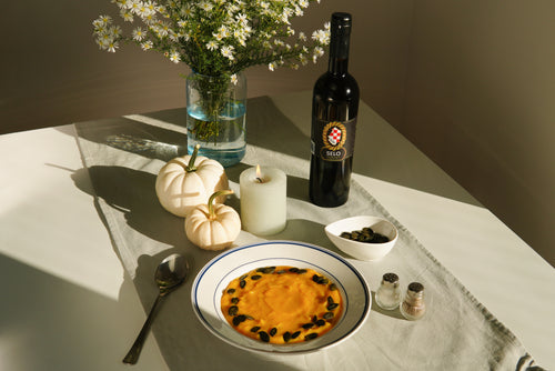 A bowl of roasted butternut squash spring dip garnished with pumpkin seeds next to a bottle of Croatian Selo extra virgin olive oil.
