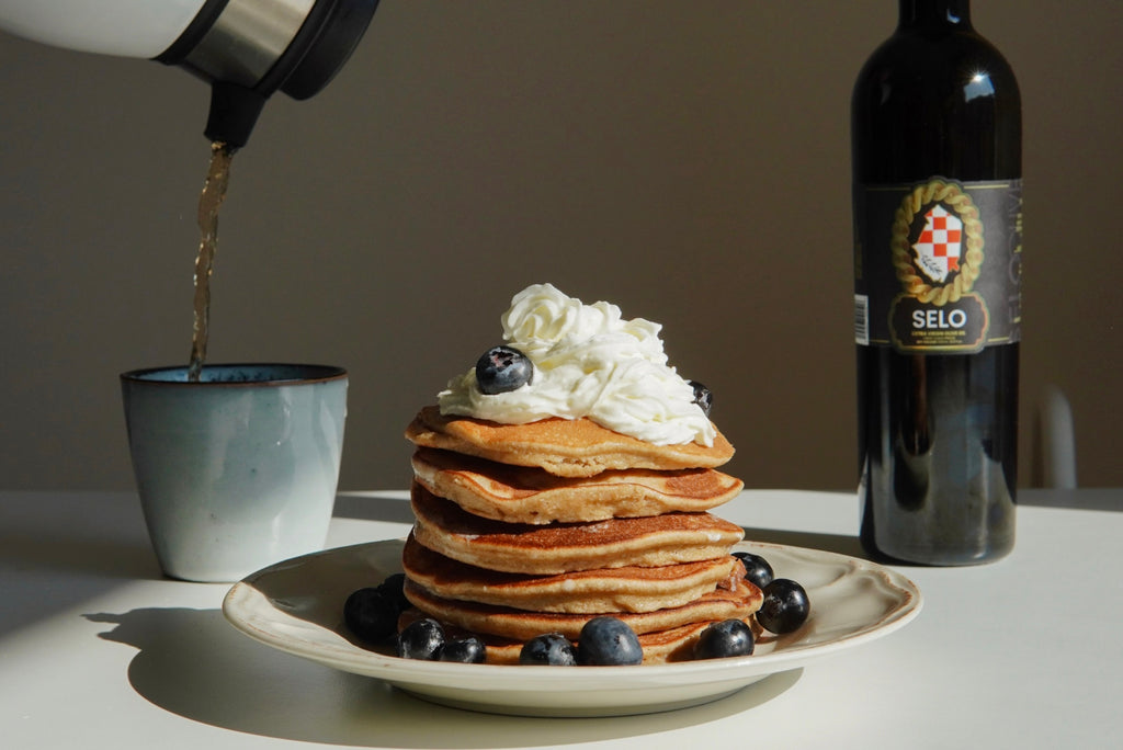 Fluffy Blueberry Pancakes served with Fresh Whipped Cream and a drizzle of Selo Croatian Extra Virgin Olive Oil, presented on a table