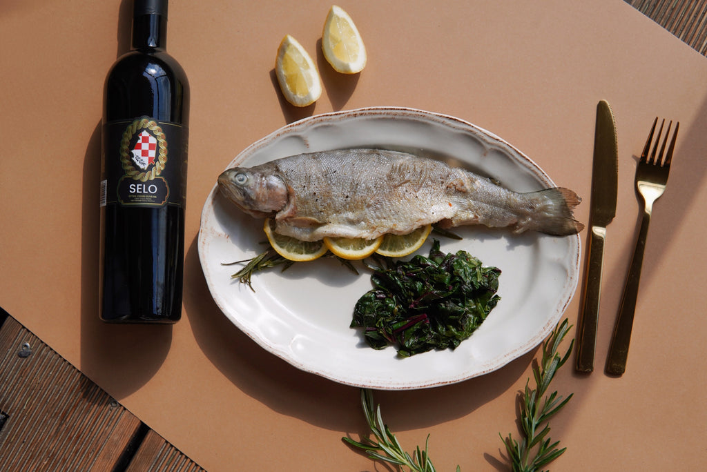 A bottle of Selo olive oil positioned next to a cooked sea bass on a dining table, illustrating its role as a keto-friendly ingredient in a healthy meal.