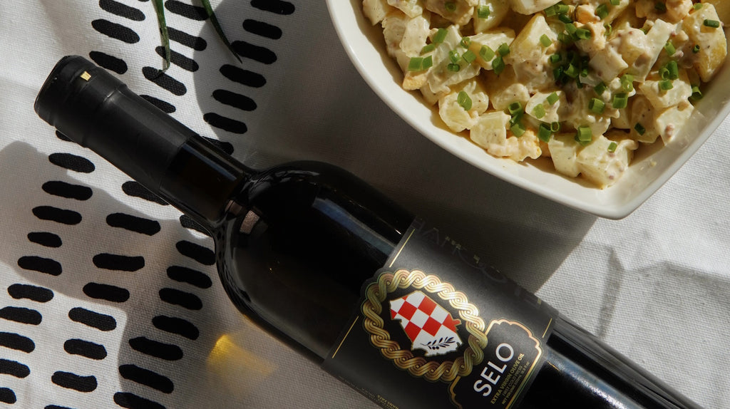 A bottle of Selo Croatian olive oil next to a colorful vegan potato salad.