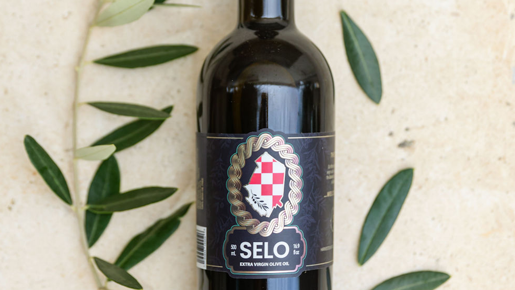 Bottle of Selo Croatian extra virgin olive oil made from Oblica olives, with fresh olive leaves on a light stone background