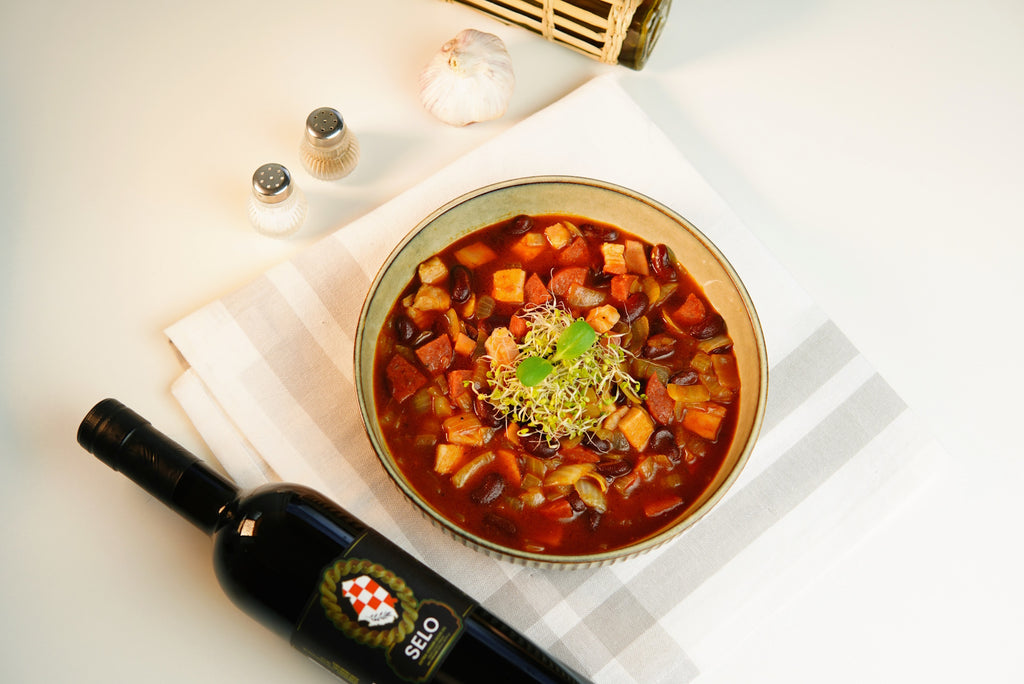 A steaming bowl of hearty Red Bean Stew (Grah i Variva), enriched with a drizzle of Croatian olive oil, offering a comforting and flavorful dish.